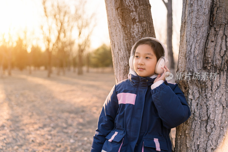 冬日暖阳在公园树林中带耳机欣赏音乐的女孩