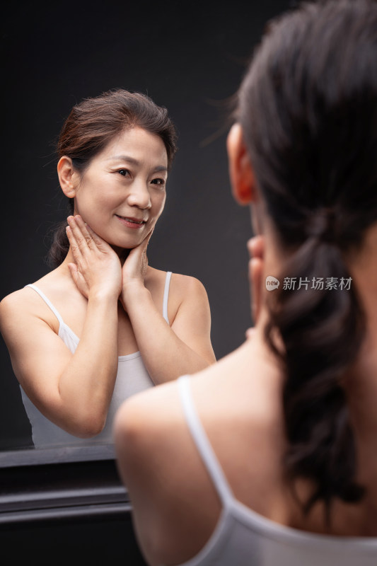 优雅的中年女人对着镜子做颈部护理