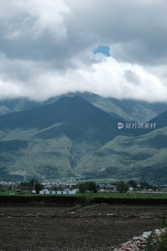 阴云下的青山远景及山脚下的土地