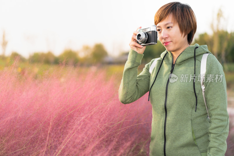 年轻的女性用相机在公园的花丛前拍照