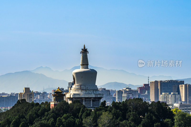 白塔矗立城市中，周边高楼与远山相映