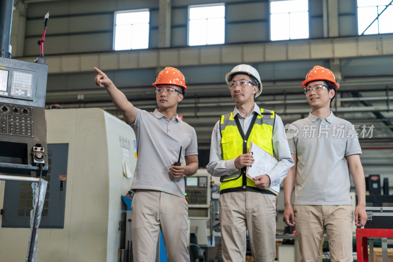 三个工程师穿保护工作服戴着安全帽在工厂工作