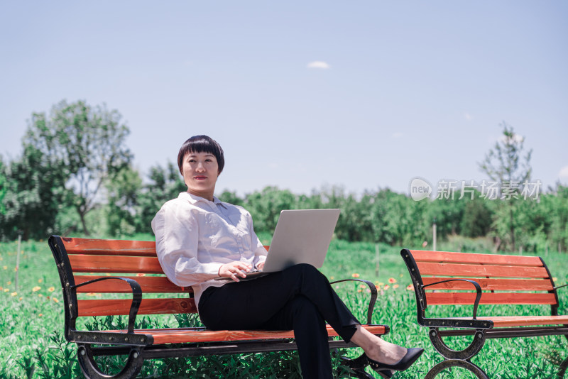 坐在长椅上使用笔记本电脑办公的地方女性
