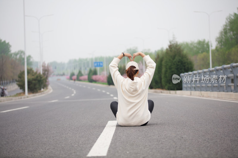 年轻的女性坐在马路中间拍摄后背照