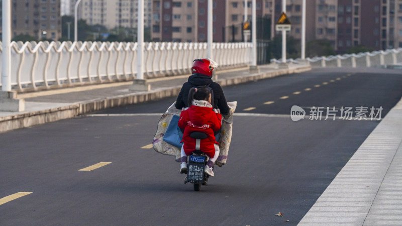 母女骑电动车行驶在宽阔道路上