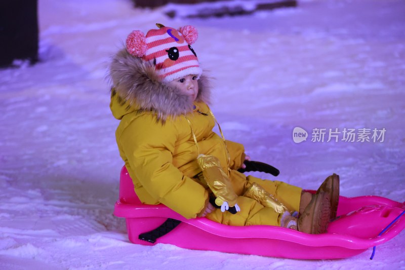 小孩雪地坐粉色雪橇