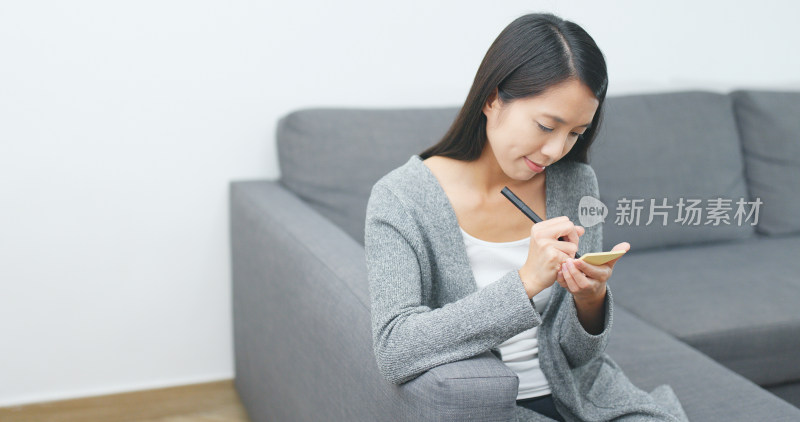 女子沙发上手持笔操作手机