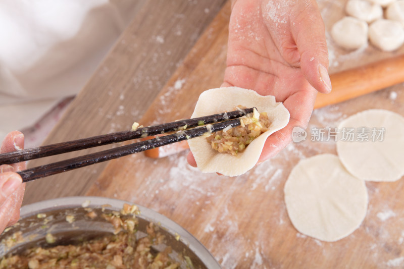 俯视拍摄筷子夹着肉馅放饺子皮上包饺子