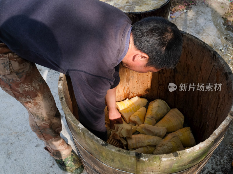 男子俯身于木桶中处理竹笋