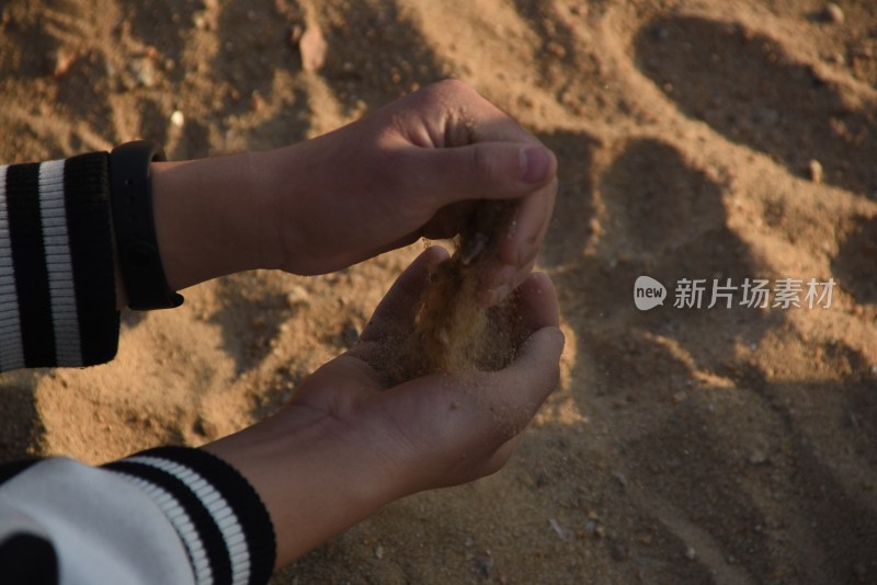 双手在沙地上捧起细沙的特写镜头