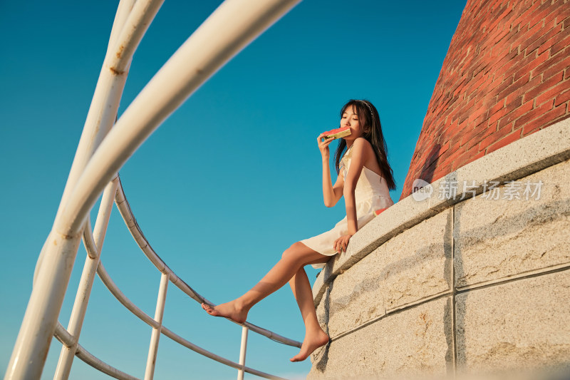 盛夏夕阳湖边码头灯塔上吃西瓜的少女