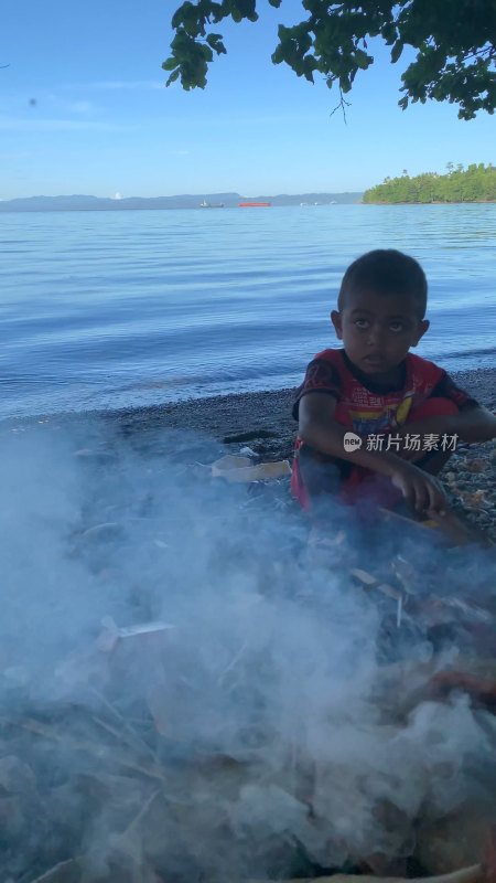 印尼当地小男孩在海边沙滩上生火