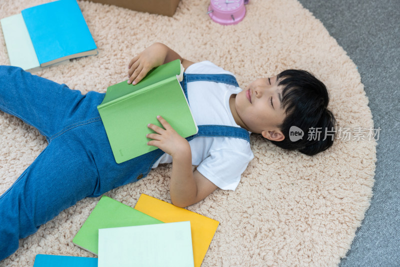 快乐的小男孩躺在地毯上看书