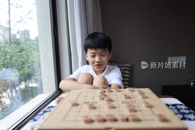 可爱的男孩在窗边下中国象棋