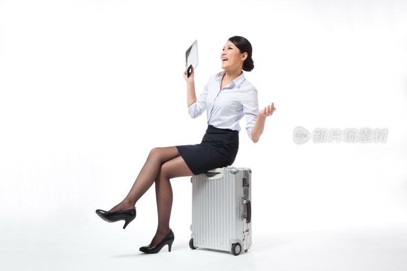 棚拍年轻商务女士坐在旅行箱上玩平板电脑