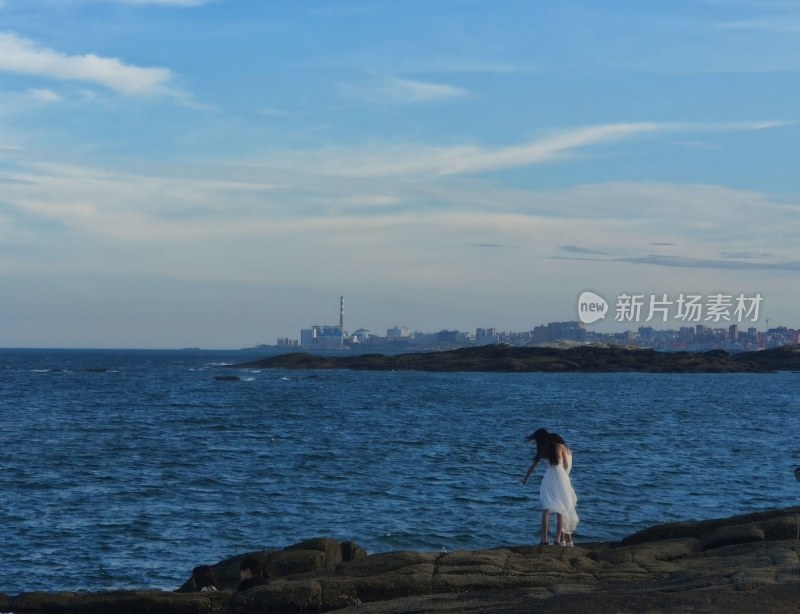 海边岩石上的白衣女子与城市远景