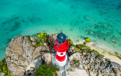 阳光下的海南三亚海岸线上礁石海浪花灯塔