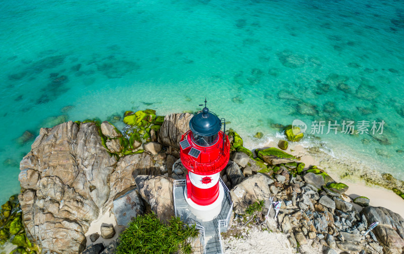 阳光下的海南三亚海岸线上礁石海浪花灯塔