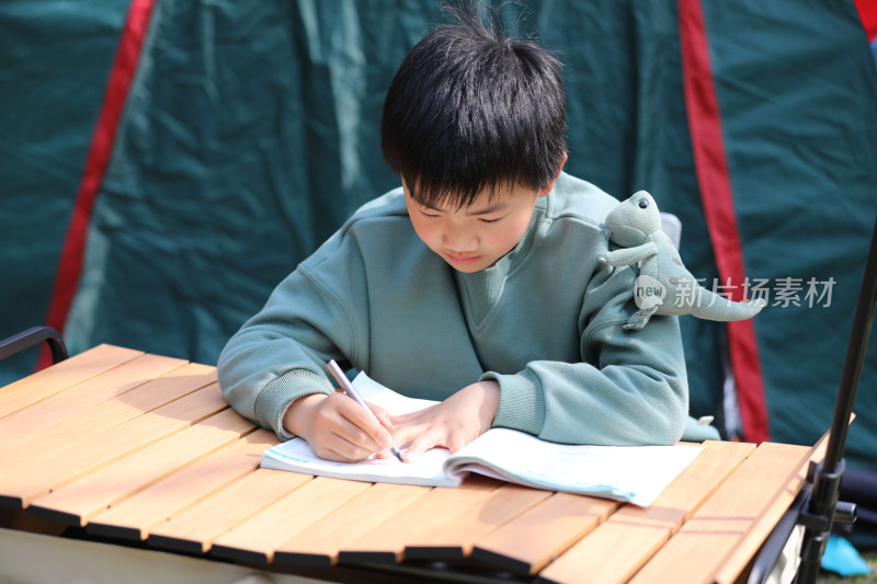 可爱的男孩在露营帐篷外写作业
