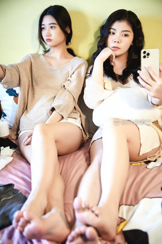 坐在床上玩手机的俩位美女