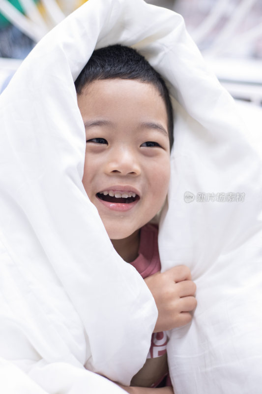 一个小男孩盖着被子在床上玩耍