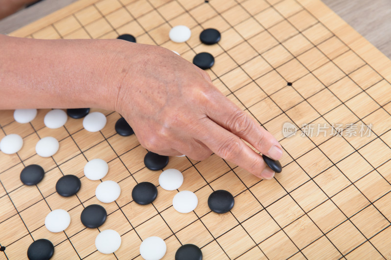 一只老人的手指夹着一枚黑色棋子下棋