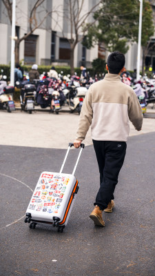 男子拉着贴满贴纸的行李箱行走在路上