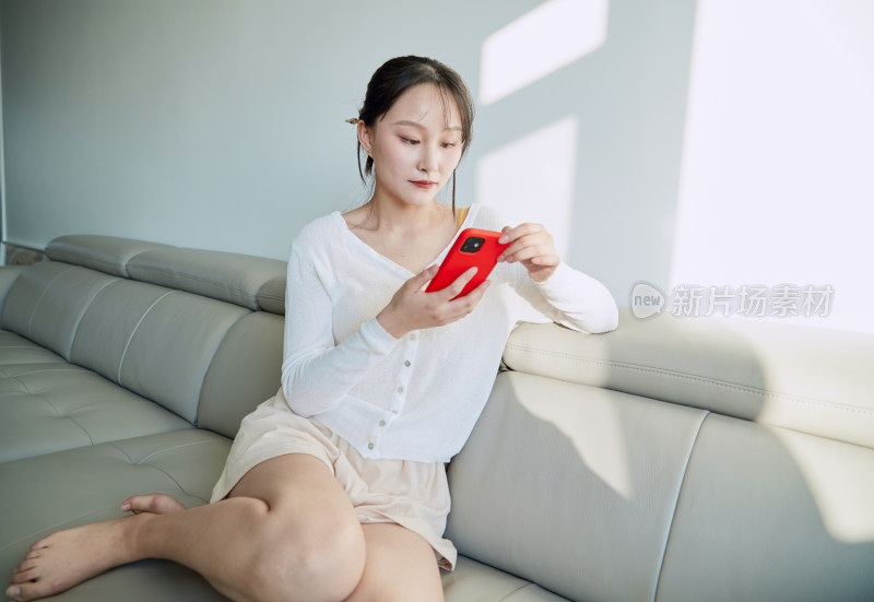 在沙发床上玩手机的年轻亚洲女性