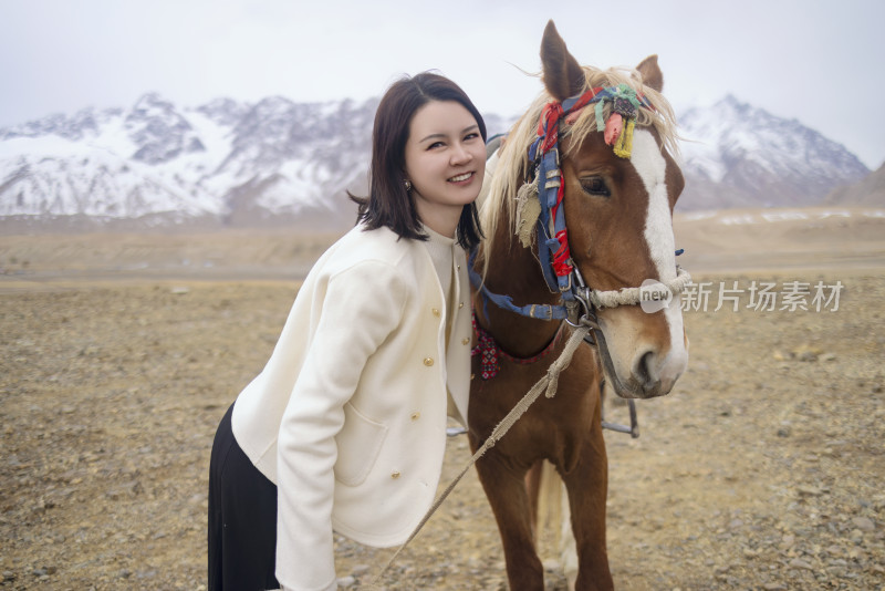 年轻女子在雪山下牵着英俊的马