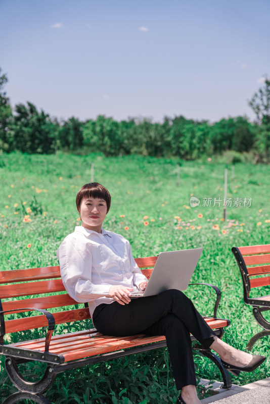 坐在长椅上使用笔记本电脑办公的地方女性