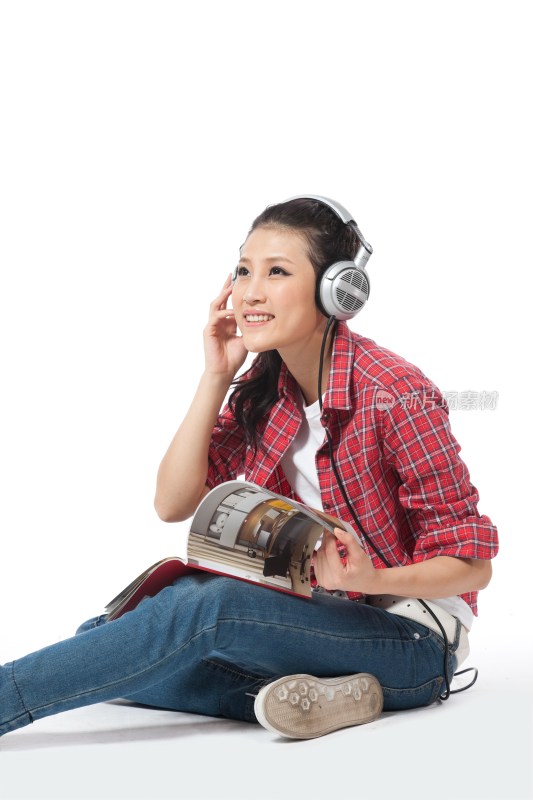 棚拍年轻女人坐在地上听音乐看杂志