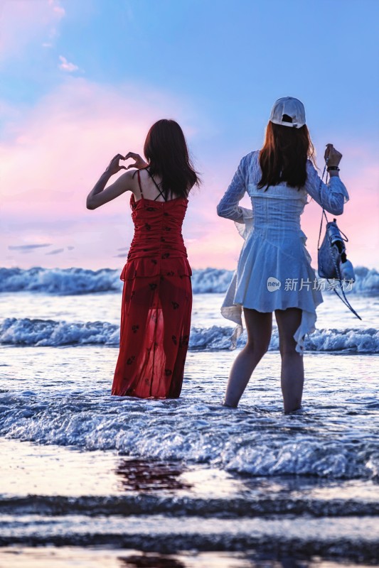 海边两位女性比心背影