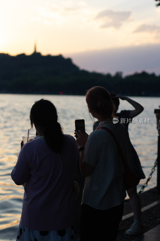 杭州西湖畔游客夕阳下拍照观景