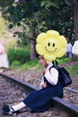 小女孩手持笑脸气球坐铁轨上的画面