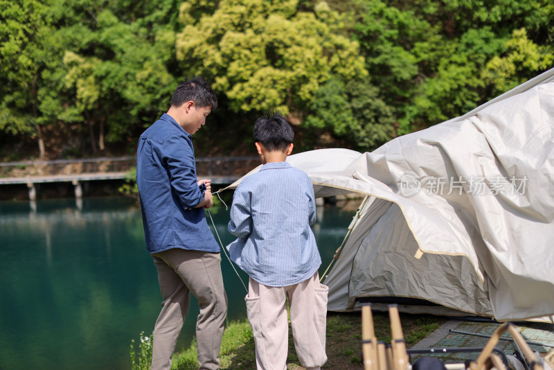 一对父子正在湖边扎帐篷