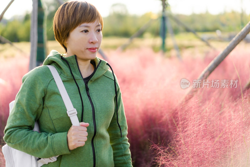 年轻的中国籍女性站在公园的花丛前