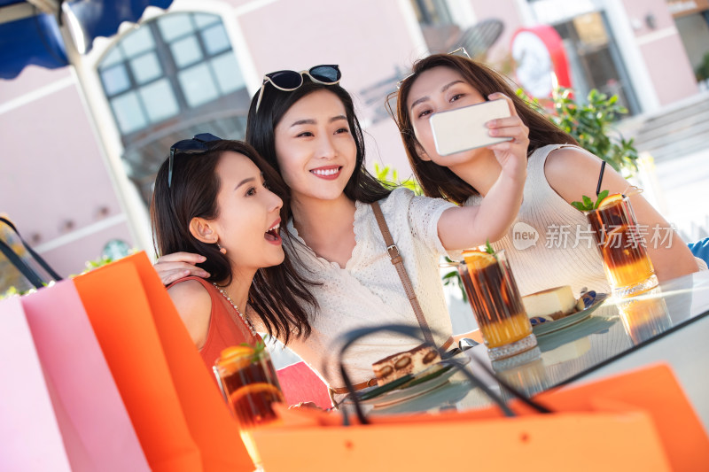 年轻女孩们坐在路边咖啡馆拿手机自拍