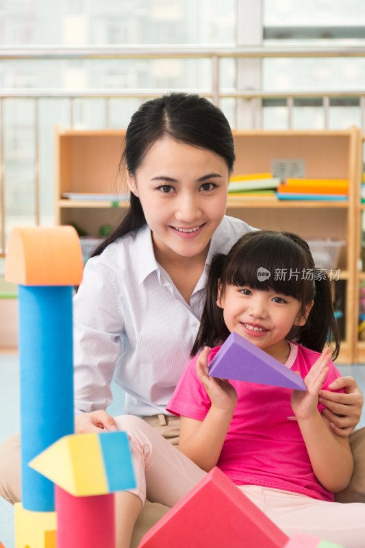 幼儿园女老师和儿童坐在地板上一起玩彩色积木
