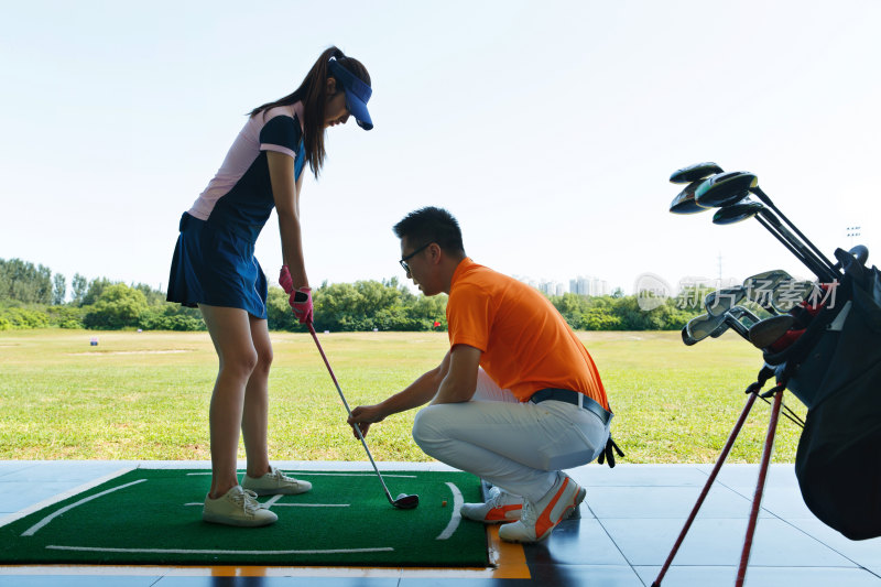 练习场上教练指导青年女人打高尔夫
