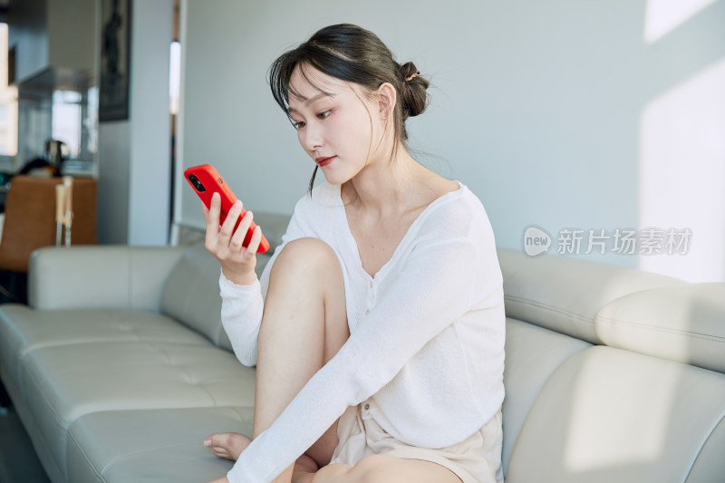 在沙发床上玩手机的年轻亚洲女性