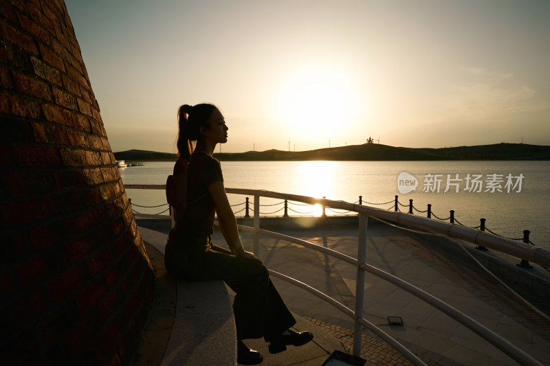 盛夏夕阳晚霞湖边码头灯塔上的少女