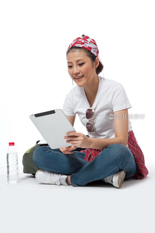 棚拍户外旅行的年轻女人坐在地上玩平板电脑
