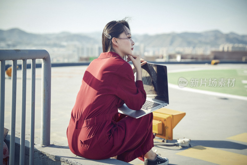 亚洲商务年轻女性在楼顶停机坪使用电脑办公