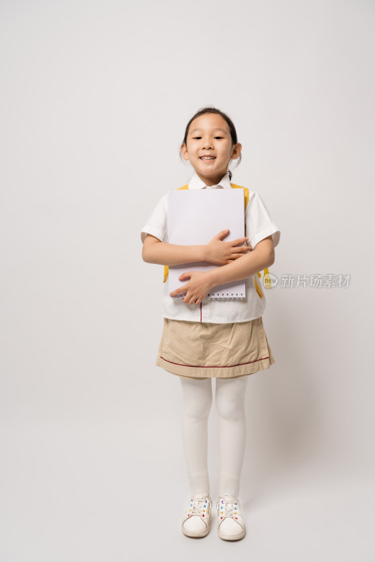 白色背景前怀抱作业本的中国女孩