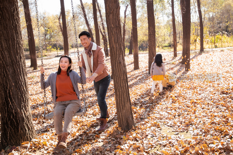 户外秋天幸福的父母在荡秋千，快乐的孩子们在旁边玩耍