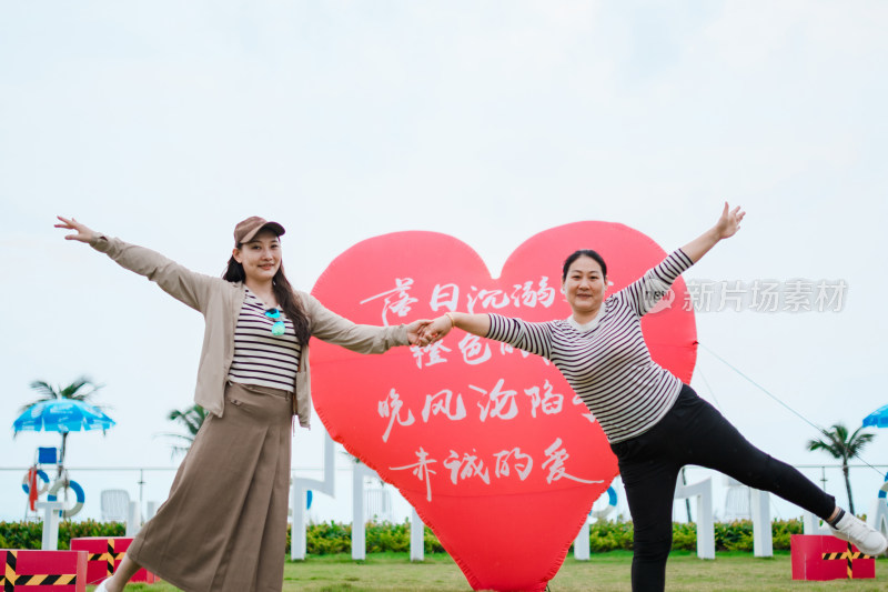 在草地上红色心形气球前开心拍照的亚洲母女