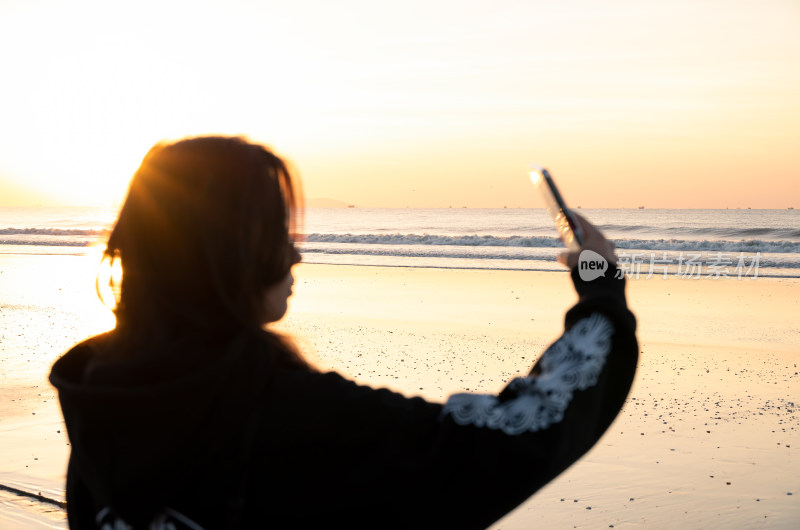 女子在海边逆光拍摄日落景象