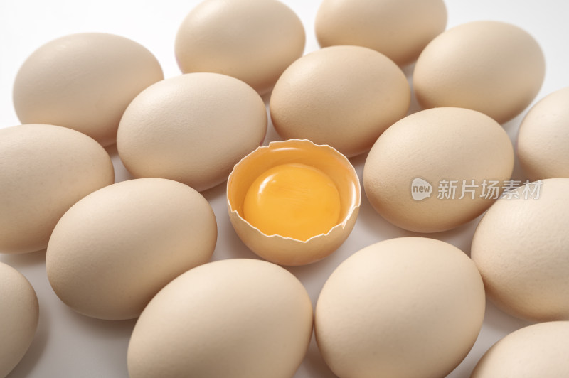 排列整齐的鸡蛋和一枚打开的露出蛋黄的鸡蛋