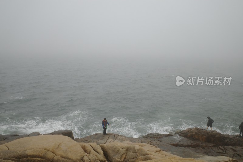 海边岩石上两人垂钓的场景