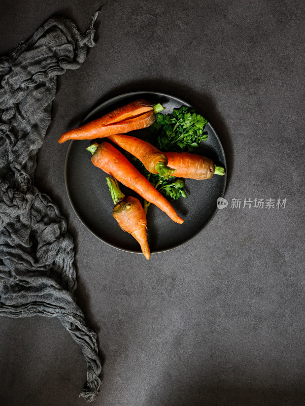 黑色桌面上，一盘子的新鲜蔬菜胡萝卜